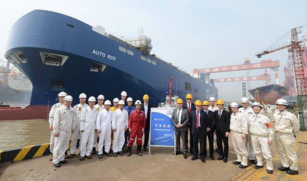Large group of staff standing at launching ceremony, on the dock in front of the Auto Eco vessel.