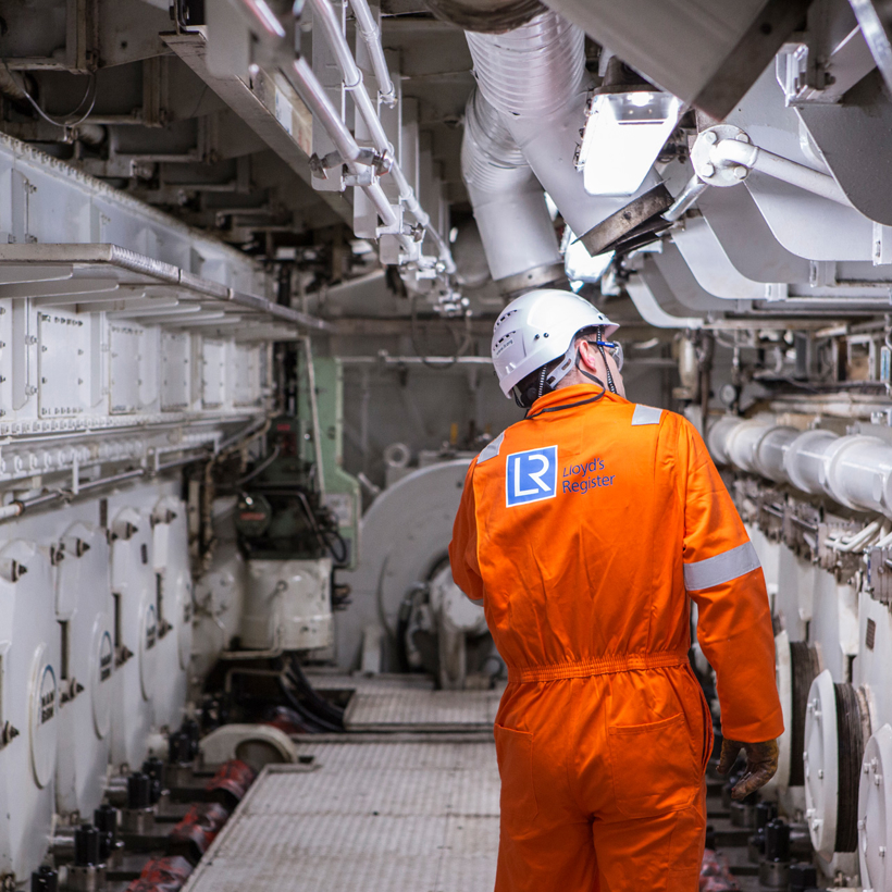 Worker in orange boiler suit surveys ship.