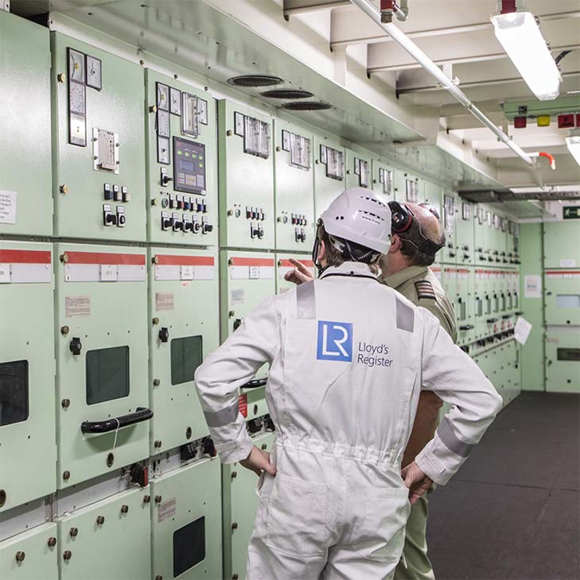 Two workers in boiler suits in the electric controls room.
