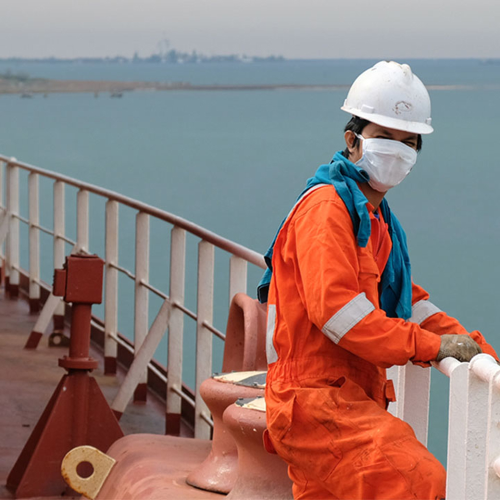 Surveyor stands on a ship wearing a hard hat, sea in the background.