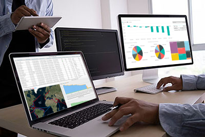 Workers sit at computer with graphs displaying on screen.