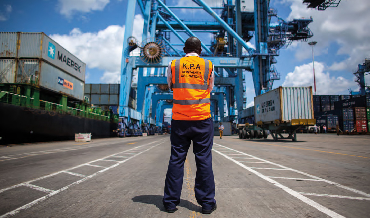 An African surveyor stands at a docking container site. 