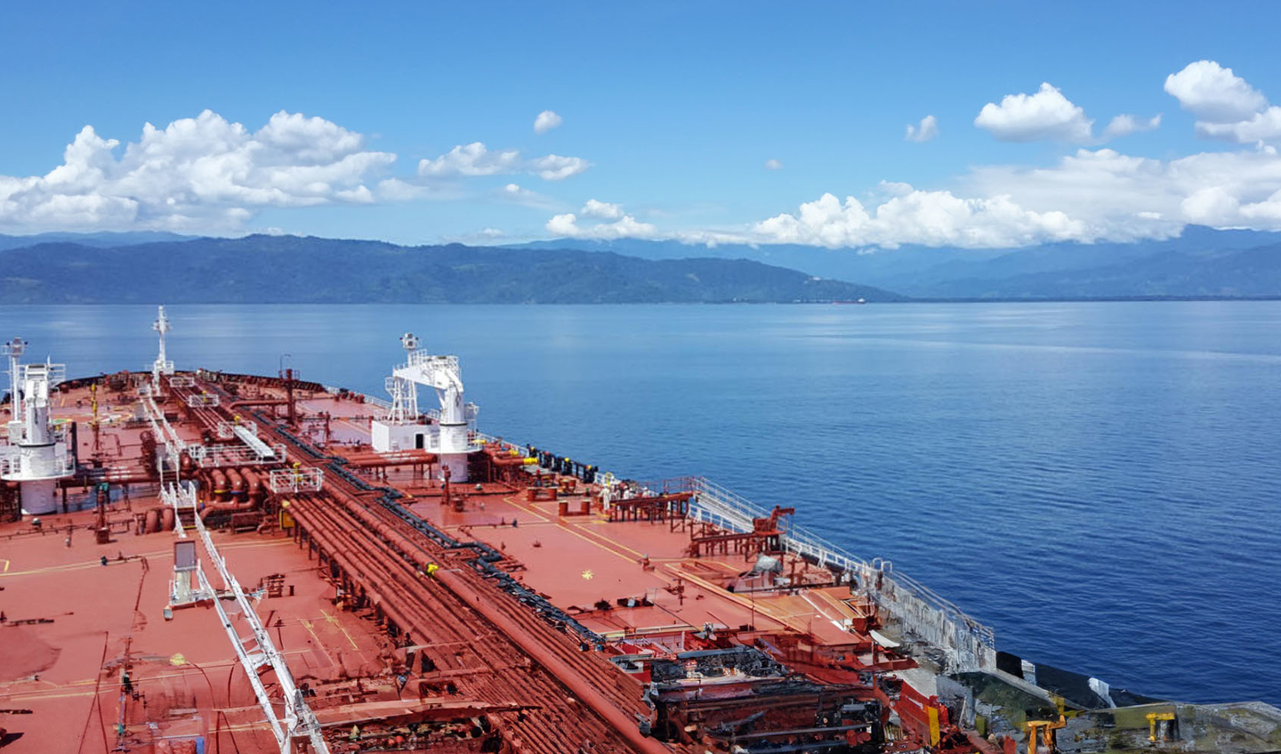 A tanker floats on the water with mountains in the background.