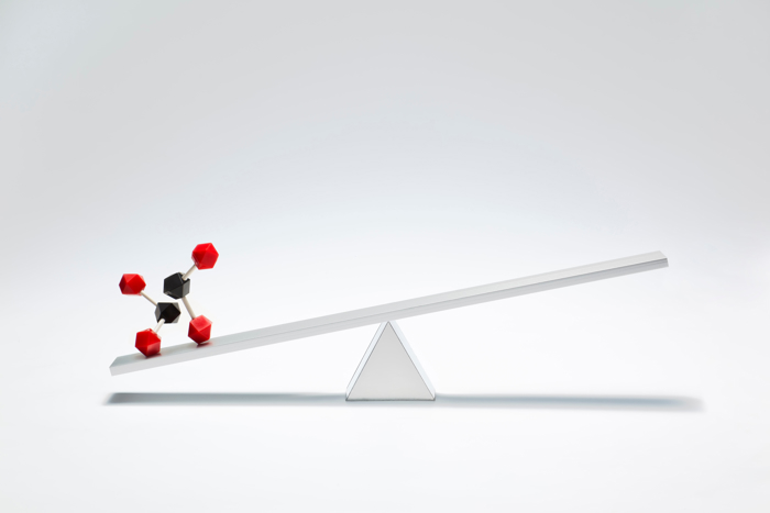 Carbon molecules balancing on a white scale.