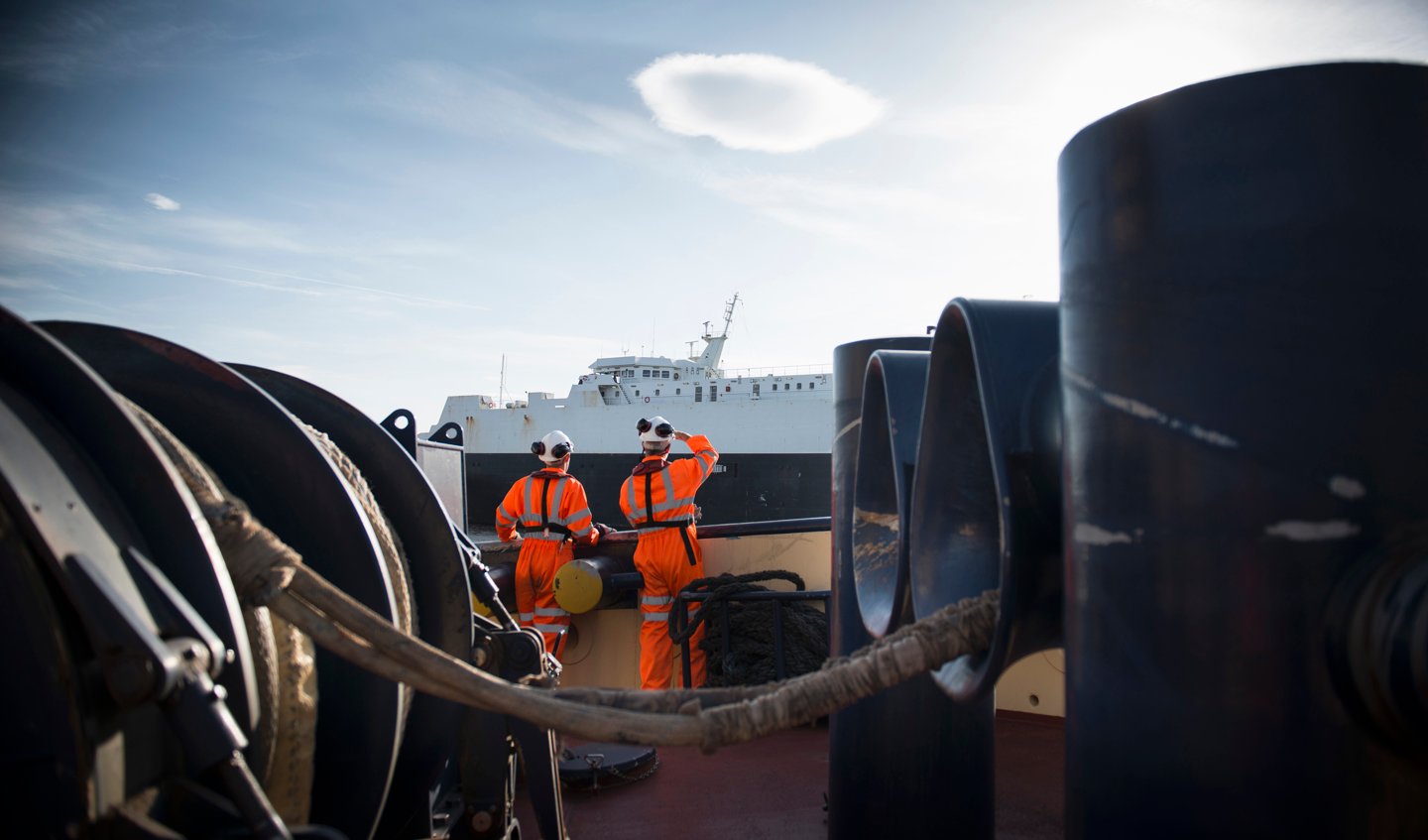 Two workers on a ship look towards another ship.