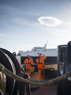 Two workers on a ship look towards another ship.