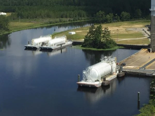 The NASA Liquid Hydrogen Barge fleet docked in waterways with a forest in the background.