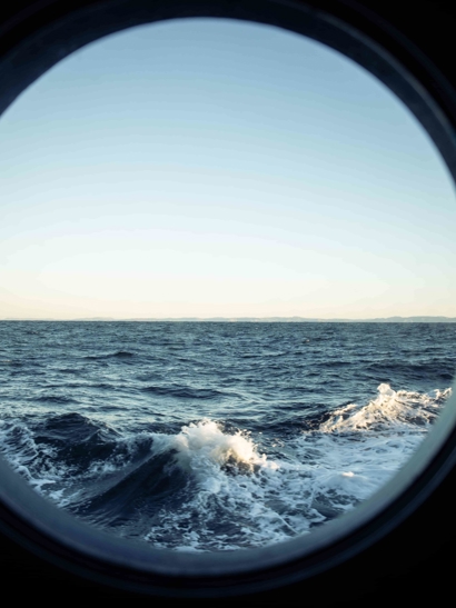 A circular ship window looks out to a wild sea. 