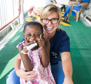 A Mercy Ships worker and an African child smile widely.