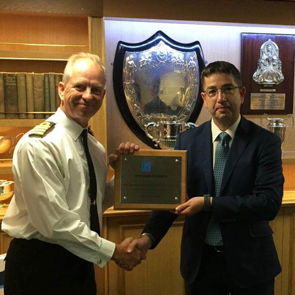 Image of class certificates being presented to the ship’s Commanding Officer by Captain Kyd in front of trophy lined wall