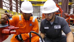 Two team members in a factory, wearing safety helmets and goggles, one is holding a torch assessing equipment.