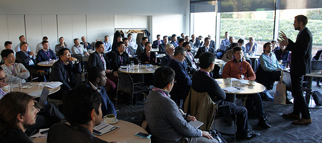 Room full of participants at a workshop sitting at tables with speaker standing up front.