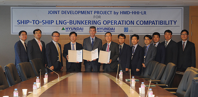 Large group photo of twelve members, three are holding the signed project documents, all standing at a boardroom table with Joint Development sign behind them.
