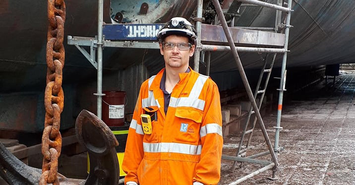 Lloyd's Register's senior surveyor Peter Hatton, in overalls, safety helmet and goggles standing in front of scaffolding.