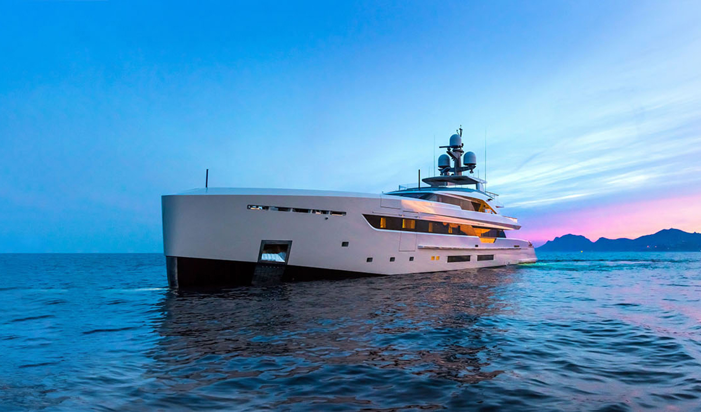 Front side view of luxury super yacht in the ocean at sunset with mountains in the background.