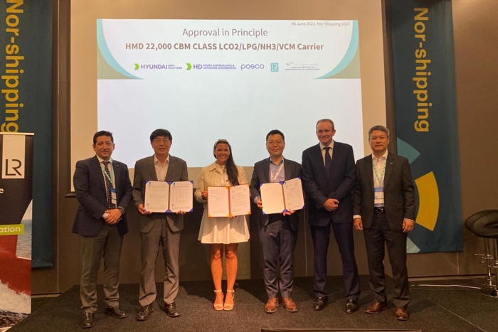 Group photo of six representatives from LR, LISCR, POSC and HMD, with three holding framed documents, standing on stage in front of Nor-Shipping signage.