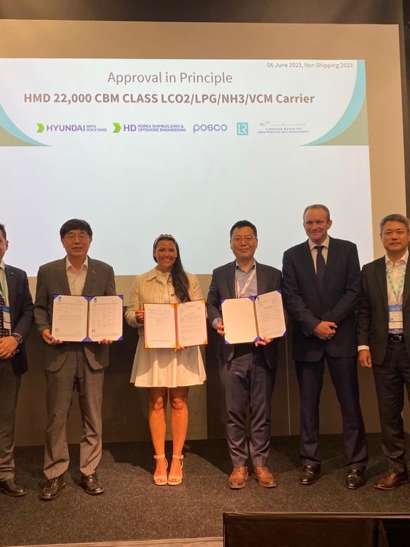 Group photo of six representatives from LR, LISCR, POSC and HMD, with three holding framed documents, standing on stage in front of Nor-Shipping signage.