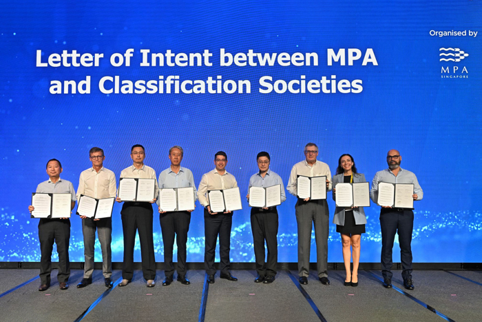 Group photo of representatives on stage holding the framed documents at the Letter of Intent ceremony.