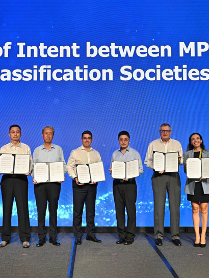 Group photo of representatives on stage holding the framed documents at the Letter of Intent ceremony.