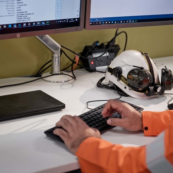Hands of someone in a high visibility boiler suit, typing at a keyboard.  The screen has LR logos on it.