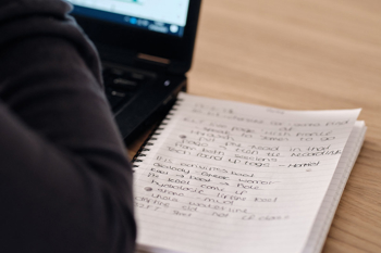 A notepad pictured next to a laptop, with the users hands in shot, intended to depict a training environment