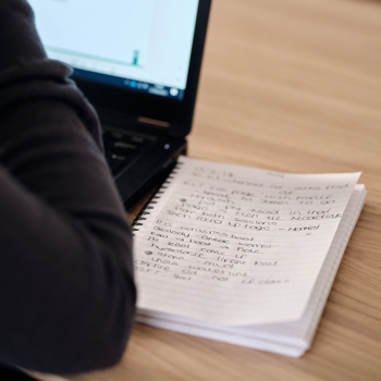 A notepad pictured next to a laptop, with the users hands in shot, intended to depict a training environment