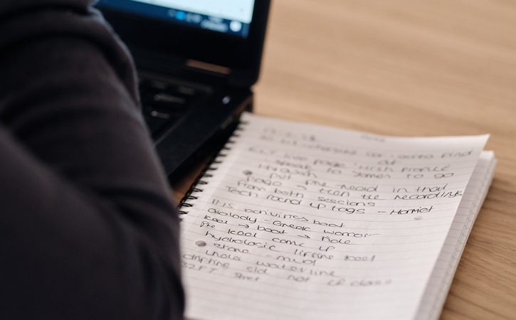 A notepad pictured next to a laptop, with the users hands in shot, intended to depict a training environment