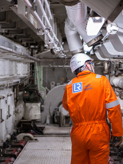 Worker in orange boiler suit surveys ship.