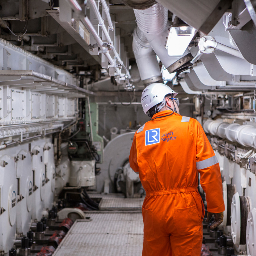 Worker in orange boiler suit surveys ship.