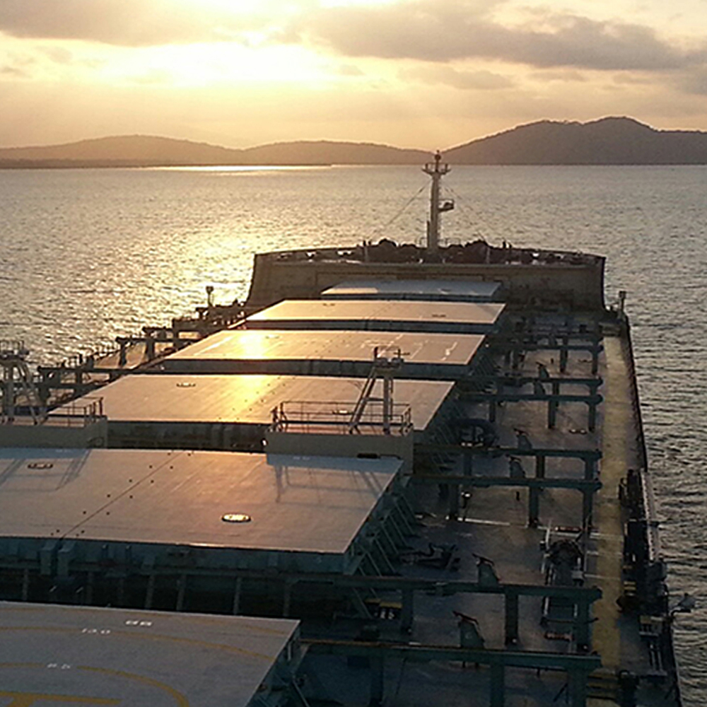 View of carrier deck out at sea at sunset with mountain range in the distance.