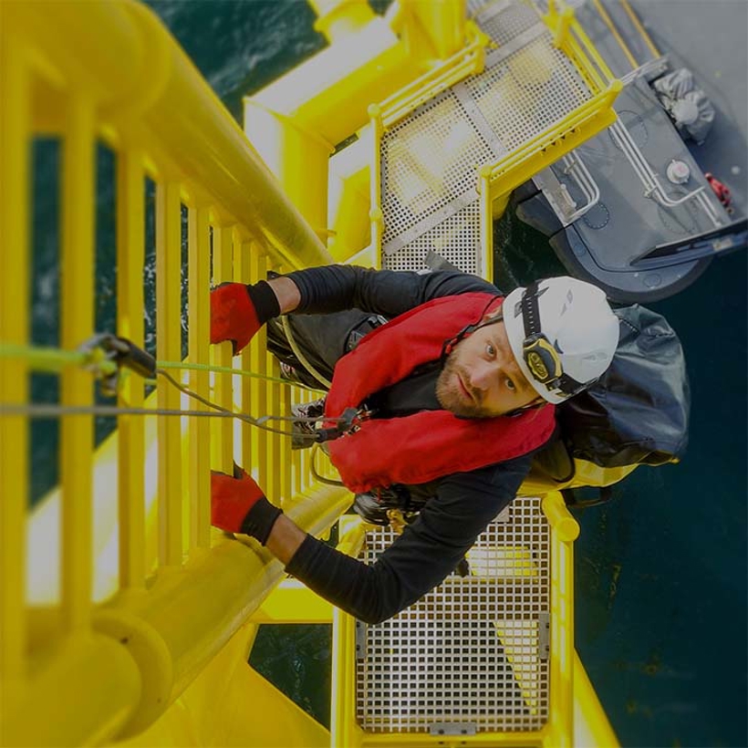 Worker in safety gear climbs wind turbine.