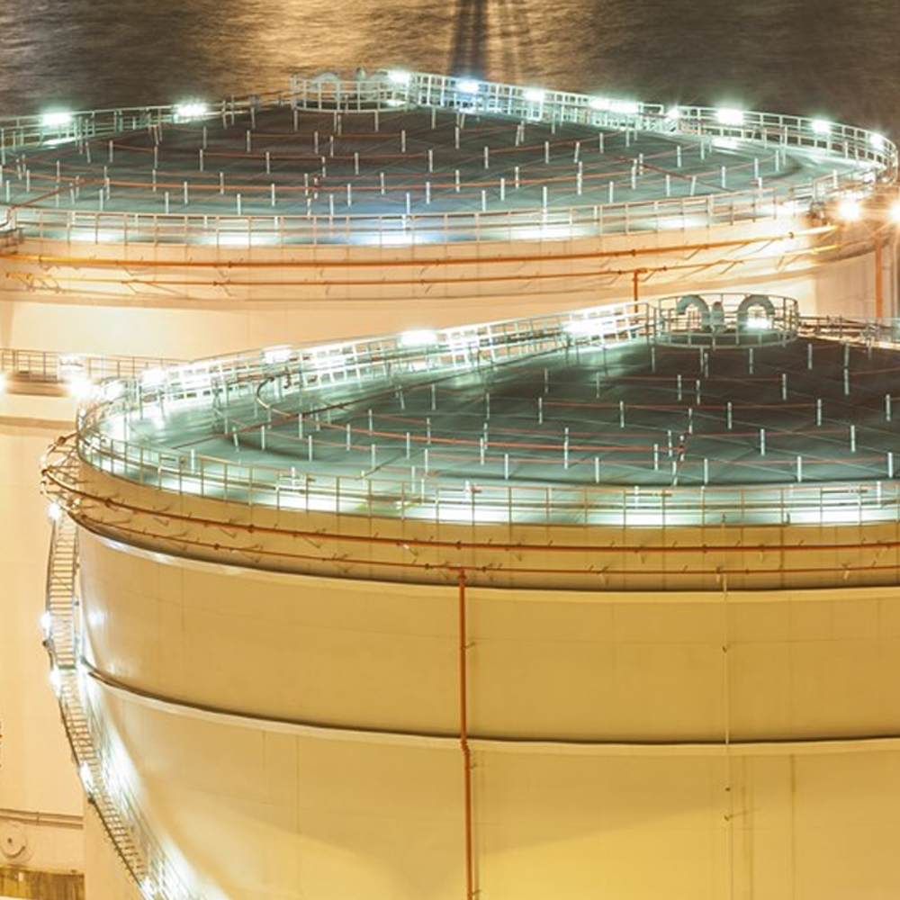 Multiple fuel silos at night with lighting along the roofs and side ladders.