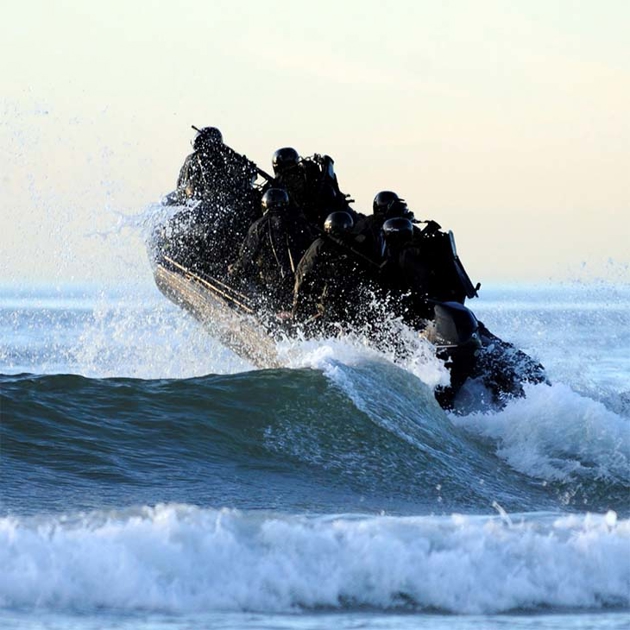 Small naval craft charges over a wave.
