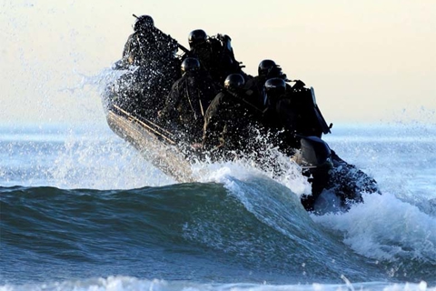 Small naval craft charges over a wave.