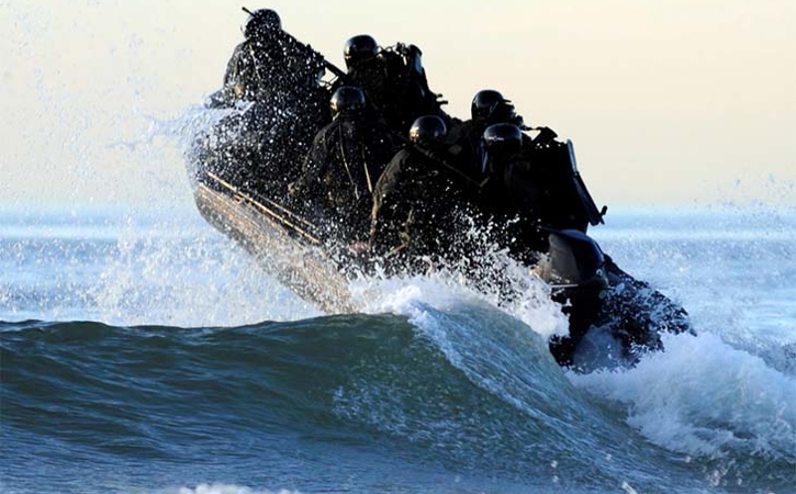Small naval craft charges over a wave.