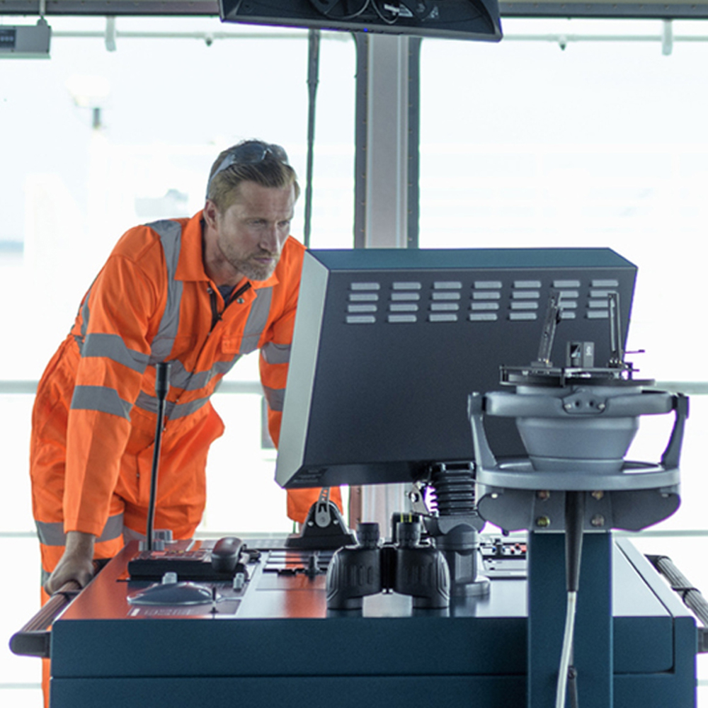 Crewman standing leaning forward on desk viewing software on a screen.