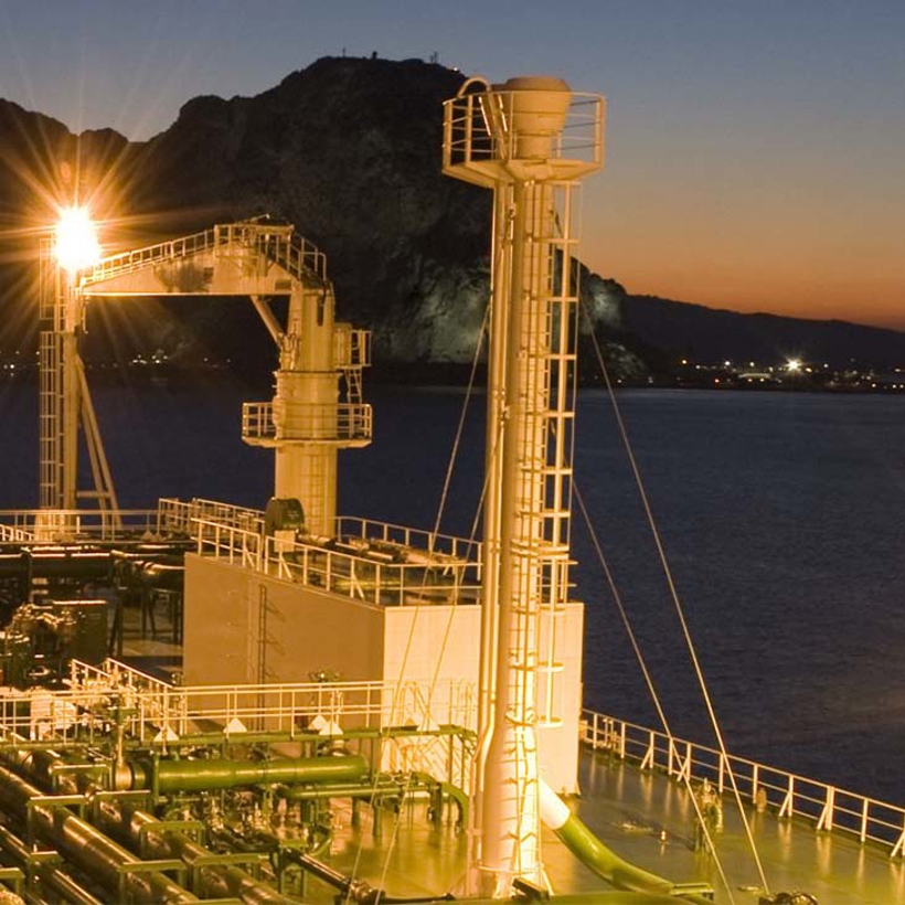 Ship lit up by lights at night, mountains in the background.
