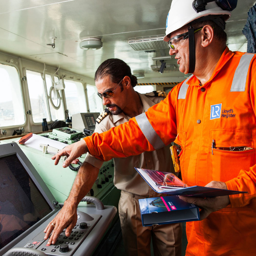 Two seafarers stand at a ships navigation desk