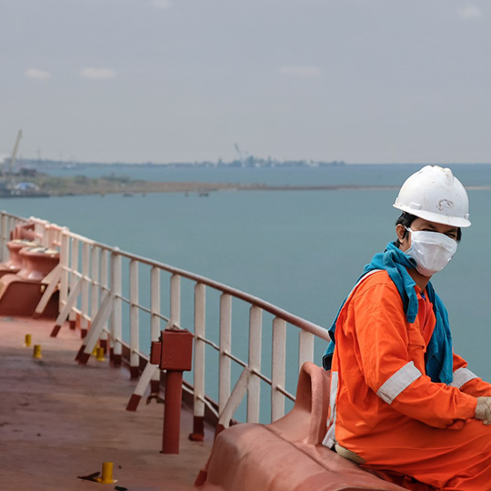 Masked seafarer sits on a ship at sea.