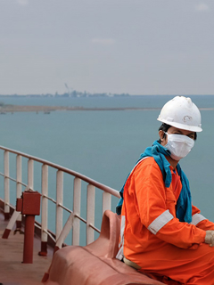 Masked seafarer sits on a ship at sea.