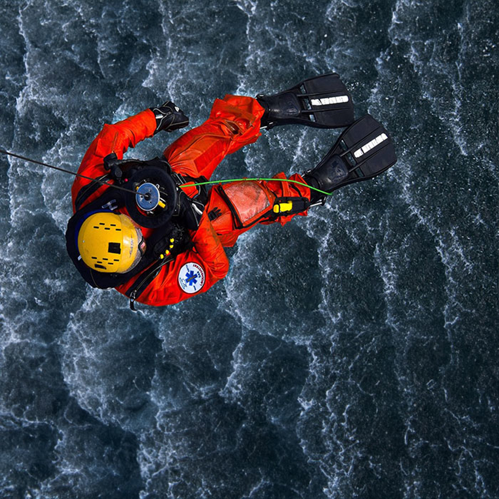 A rescue worker in action hangs from a helicopter cable over the ocean.